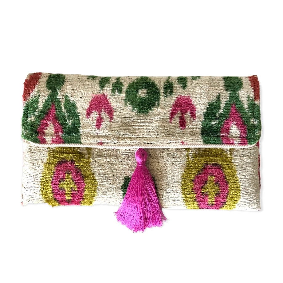 Handwoven silk velvet clutch with ikat pattern in cream, green, pink, and gold, featuring decorative pink tassel closure
