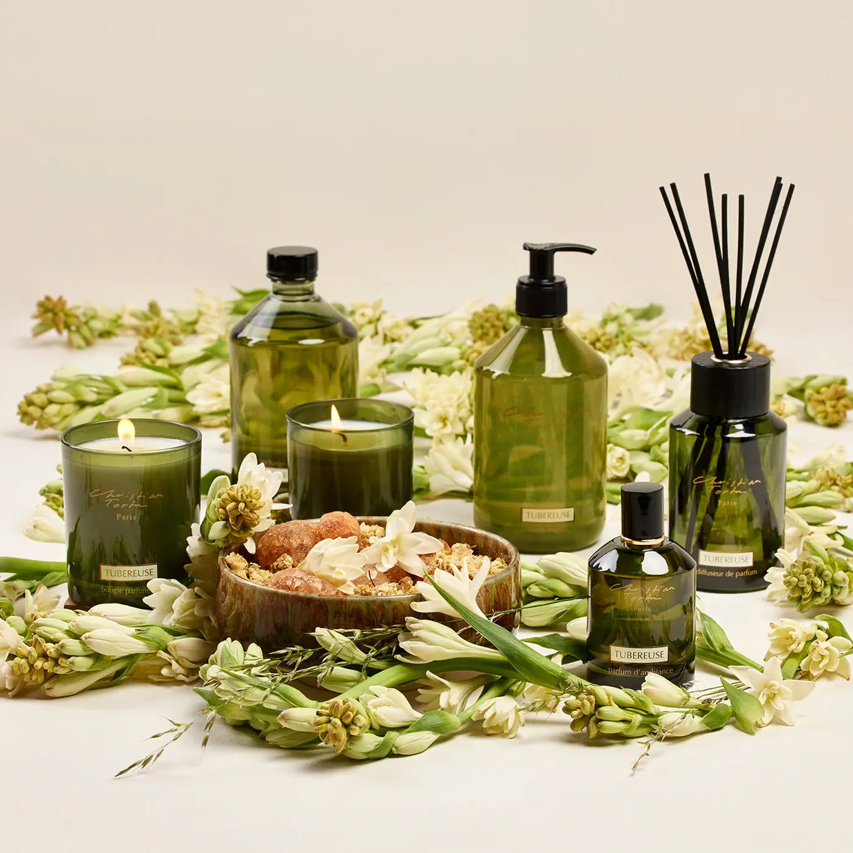 Tuberose fragrance collection in olive green glass bottles with black caps, surrounded by white tuberose flowers on cream backdrop