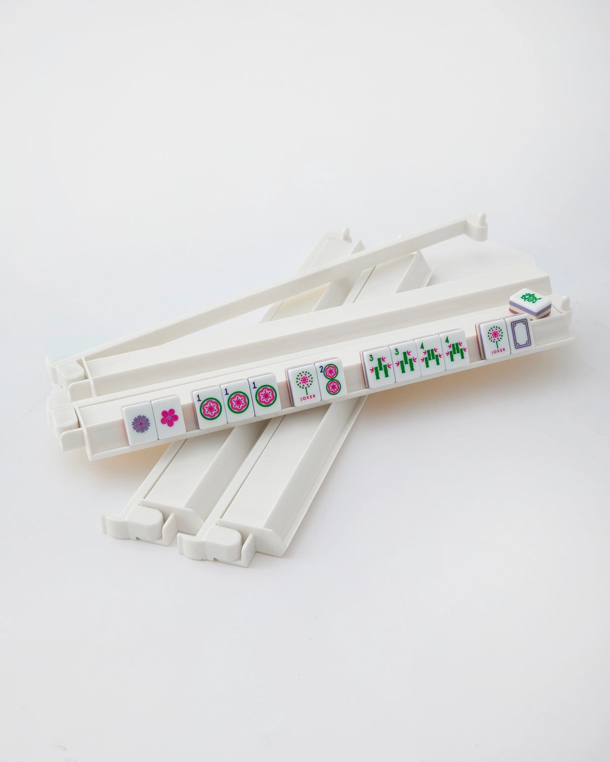 White plastic mahjong tile racks with colorful tiles showing flowers, circles, bamboo and character suits arranged diagonally