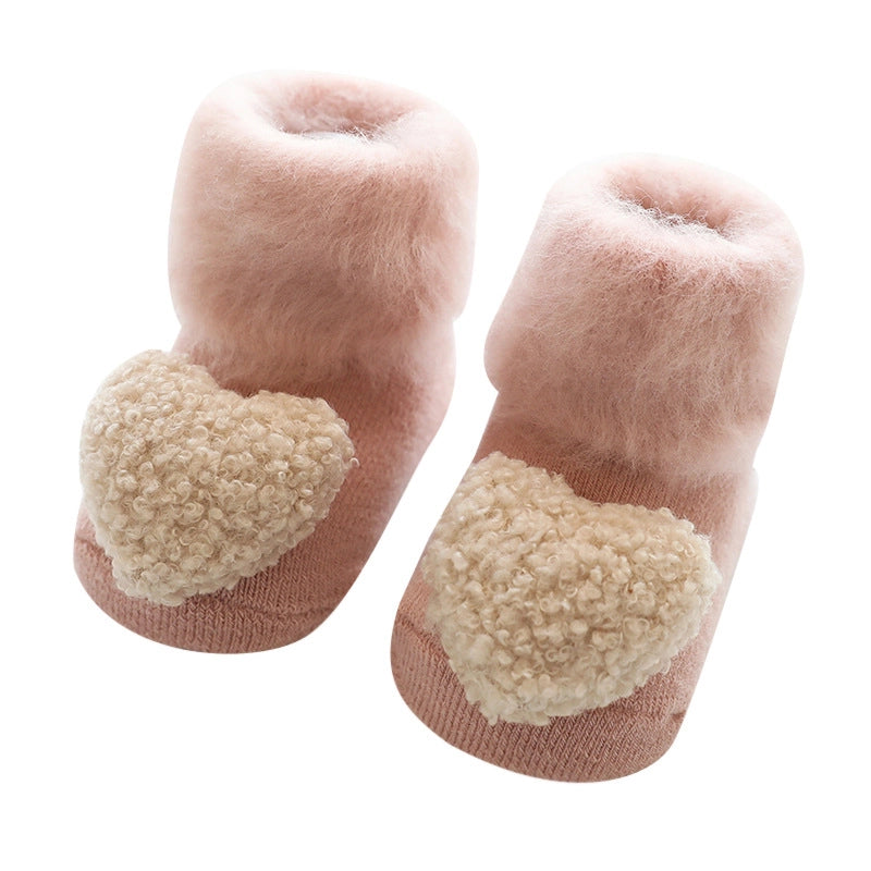 Blush pink fuzzy baby booties with cream textured pom-poms on top and fold-over cuffs on white background