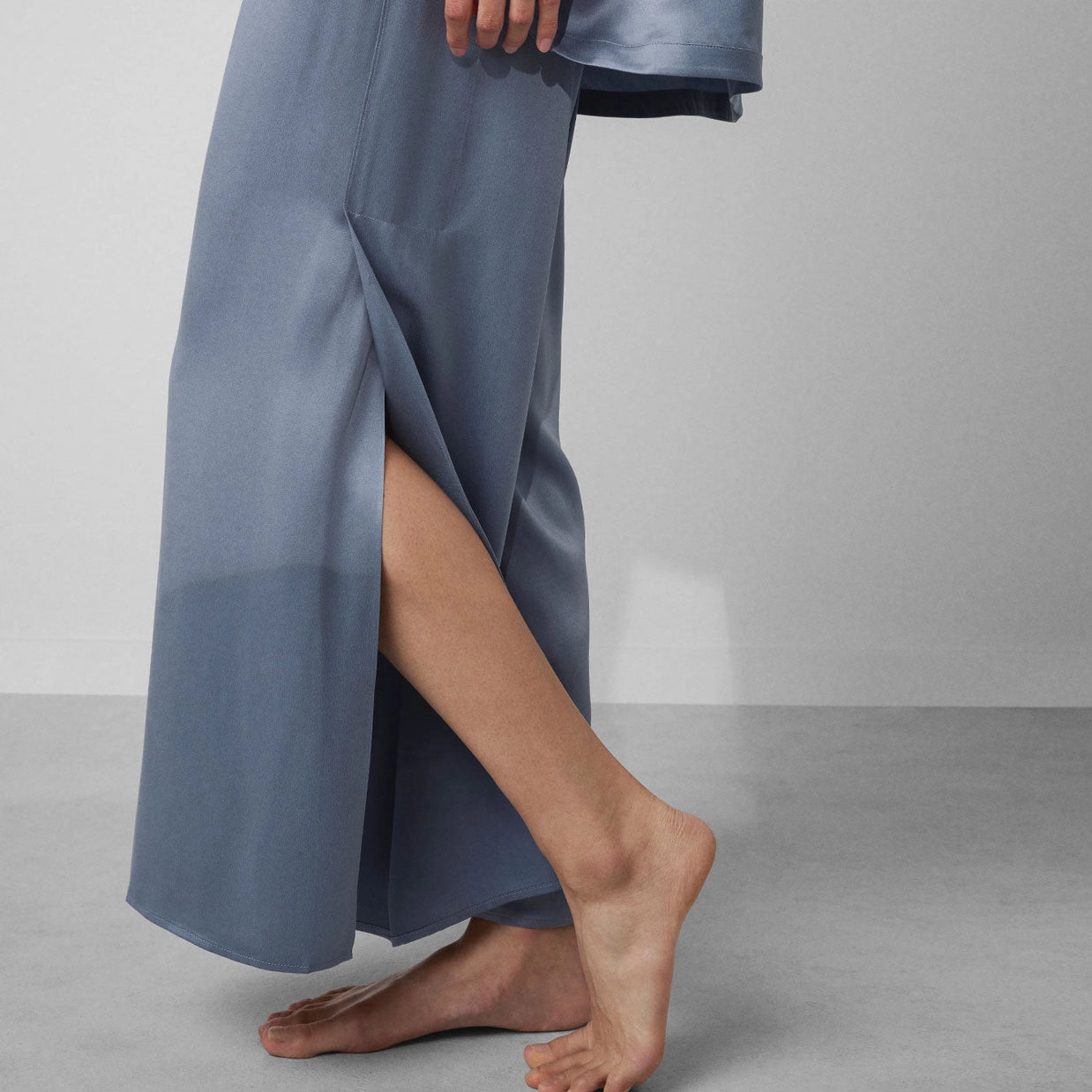 Slate blue satin lounge pants with side slit detail shown on model walking barefoot against gray backdrop