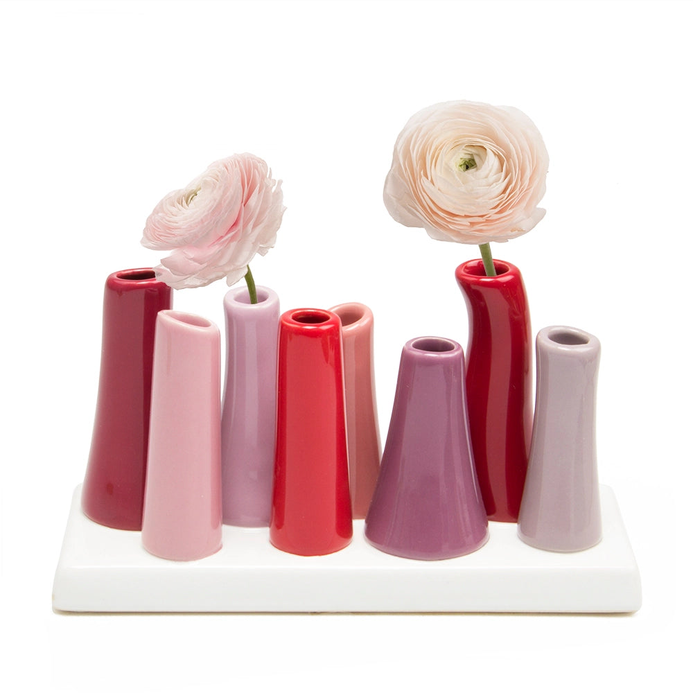 Multi-tube ceramic vase set in pink and red tones on white base with two ranunculus flowers in pale pink and peach