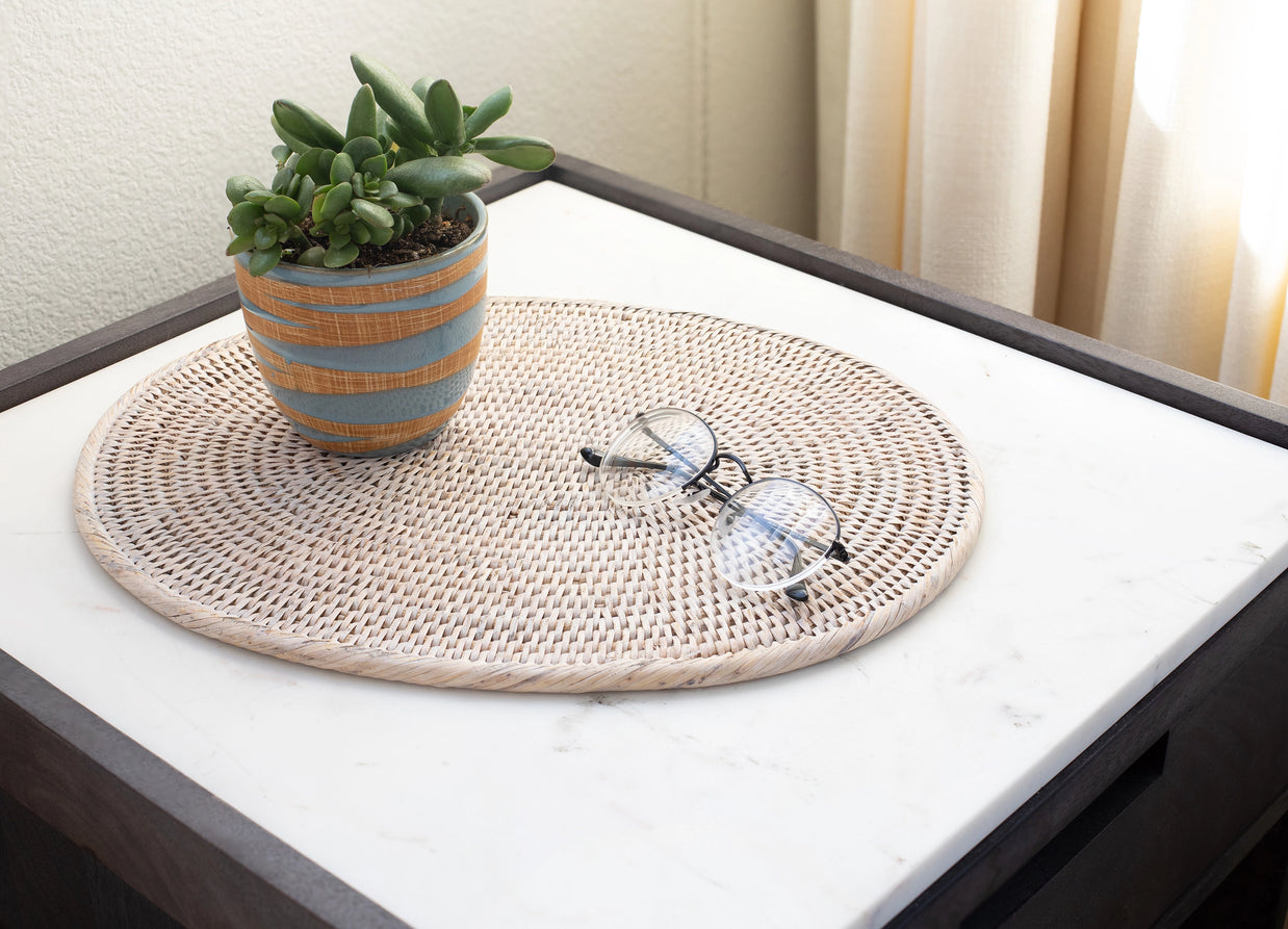 Round woven rattan tray in natural tan with spiral weave pattern holding succulent pot and reading glasses on white surface
