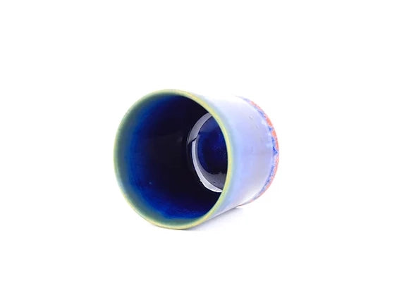 Handmade ceramic cup in periwinkle blue with deep cobalt blue interior glaze, viewed from above at angle on white background