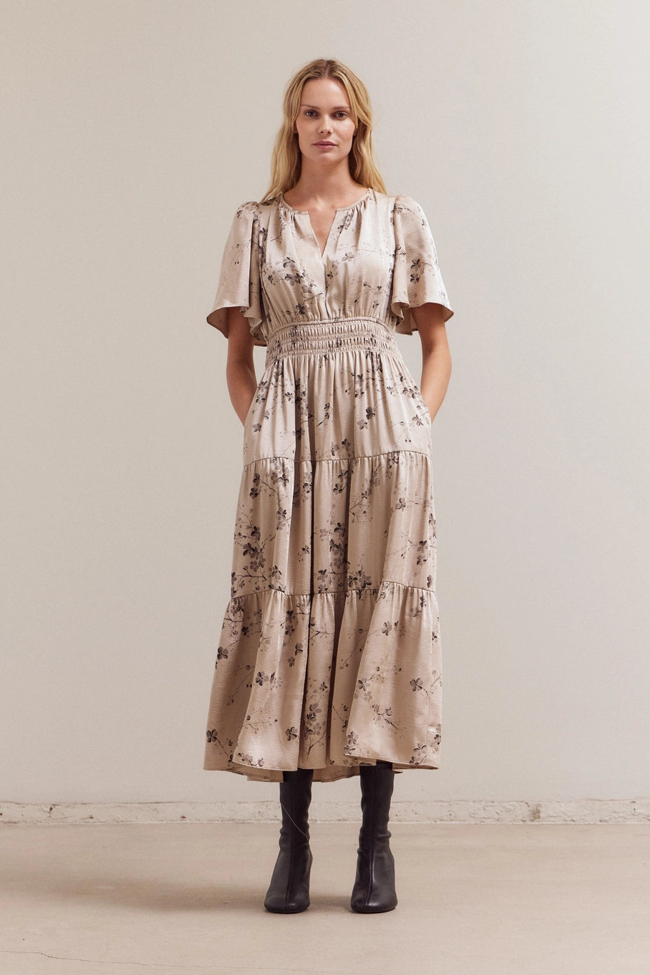 Beige tiered maxi dress with brown floral print, flutter sleeves, smocked waist, and split neckline with flowing silhouette