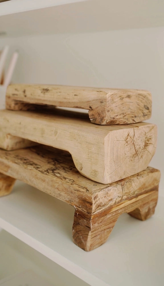Stack of three rustic natural wood risers with carved feet showing grain patterns and weathered texture on white shelf