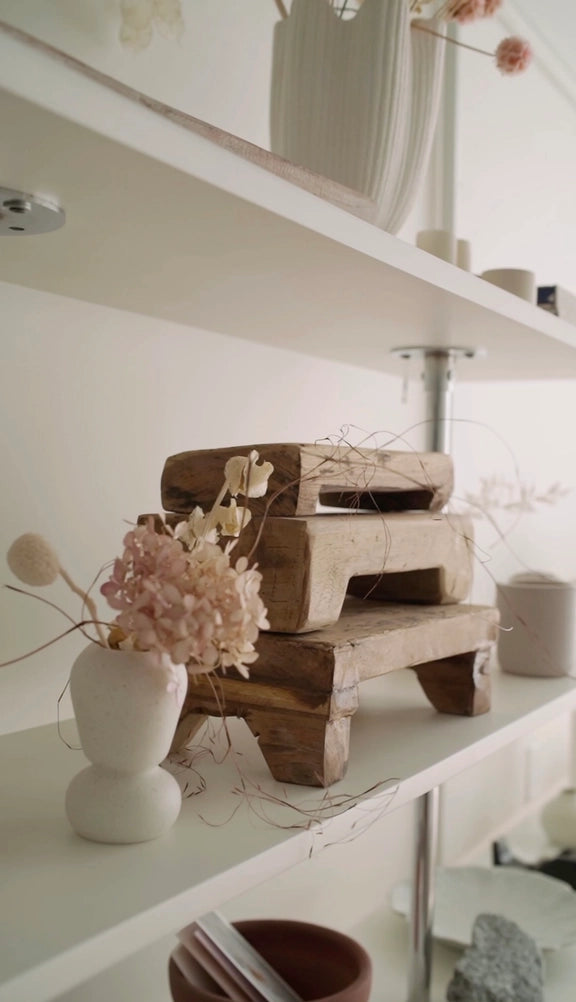 Stacked reclaimed wood brick forms displayed on white shelf with cream bubble vase holding dried pink hydrangea stems
