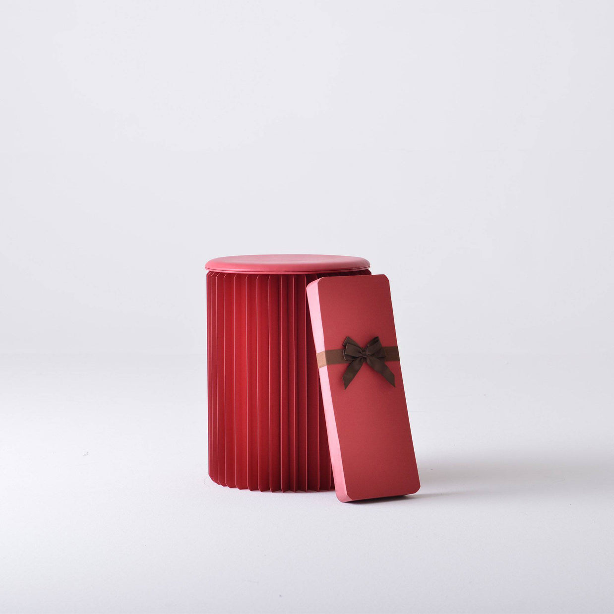 Red cylindrical storage tin with vertical ribbed texture and smooth lid, pink gift card with burgundy bow leaning against it
