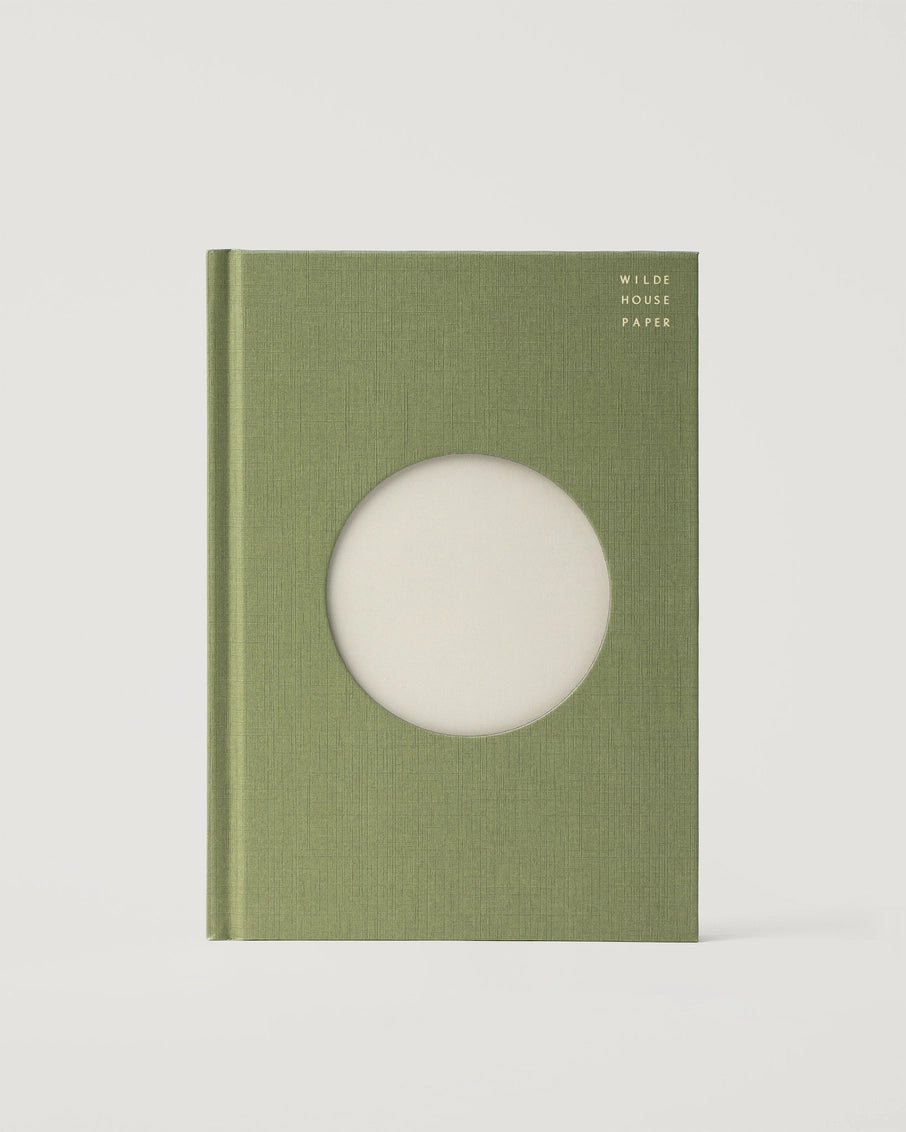 Sage green linen hardcover journal with circular cutout window revealing cream pages, titled "Wilde House Paper" in gold text