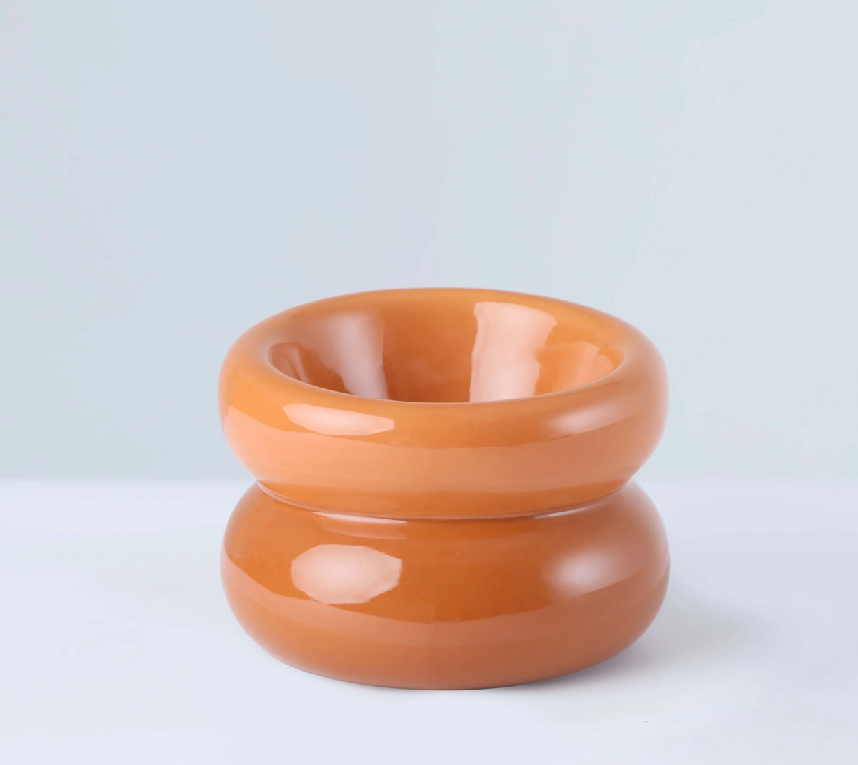 Glossy peachy-orange ceramic donut-shaped bowl with smooth rounded curves and central opening on reflective surface