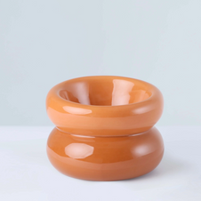 Glossy peachy-orange ceramic donut-shaped bowl with smooth rounded curves and central opening on reflective surface