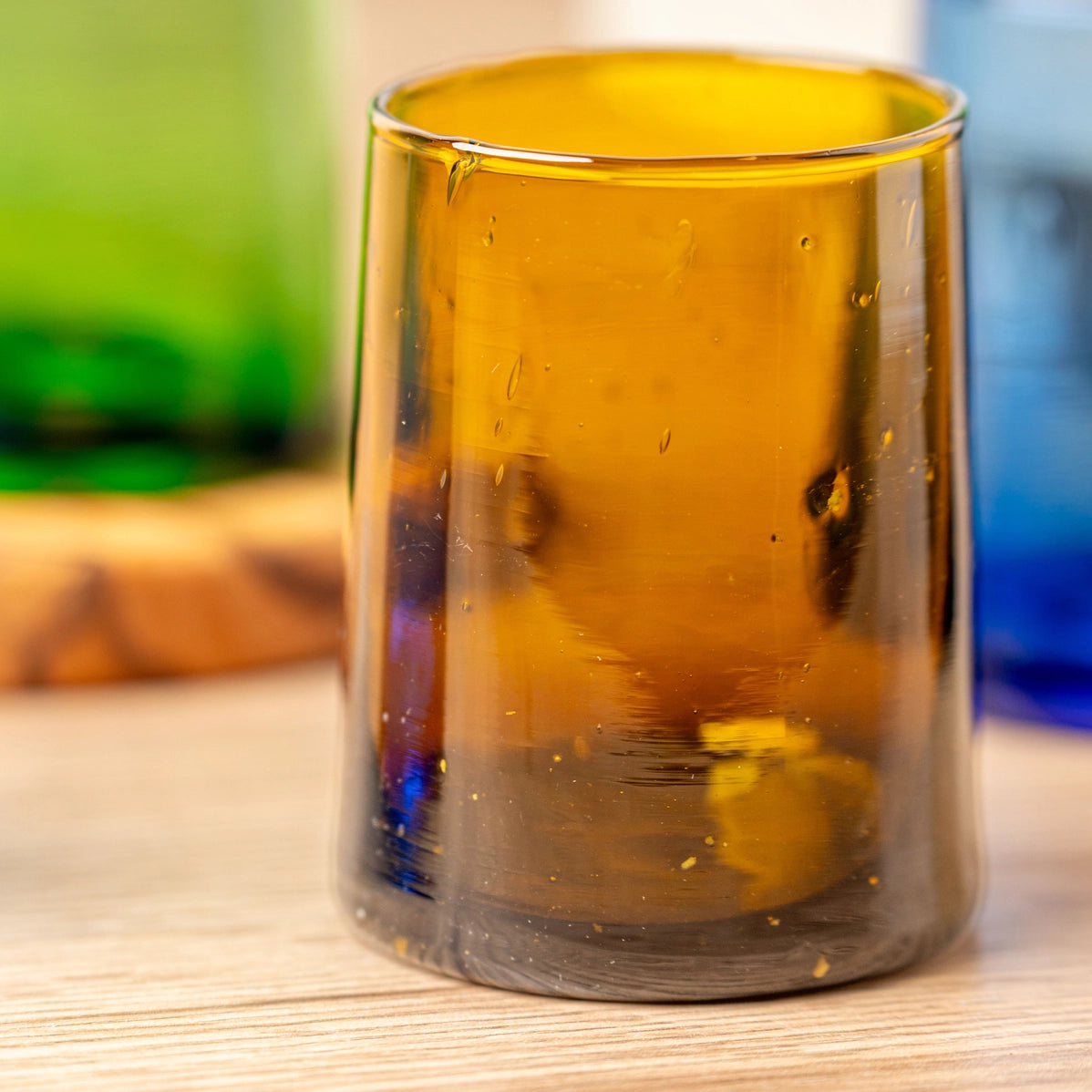 Handblown amber glass tumbler with tapered cone shape and visible bubbles, featuring warm golden-orange translucent color