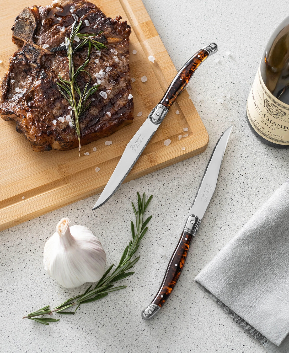 Stainless steel steak knives with tortoiseshell resin handles and folding mechanism on speckled quartz countertop
