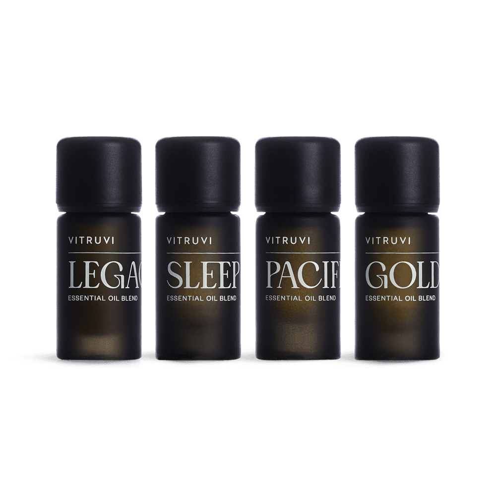 Four dark amber glass bottles with black caps labeled Vitruvi essential oil blends in Legacy, Sleep, Pacific, and Gold varieties
