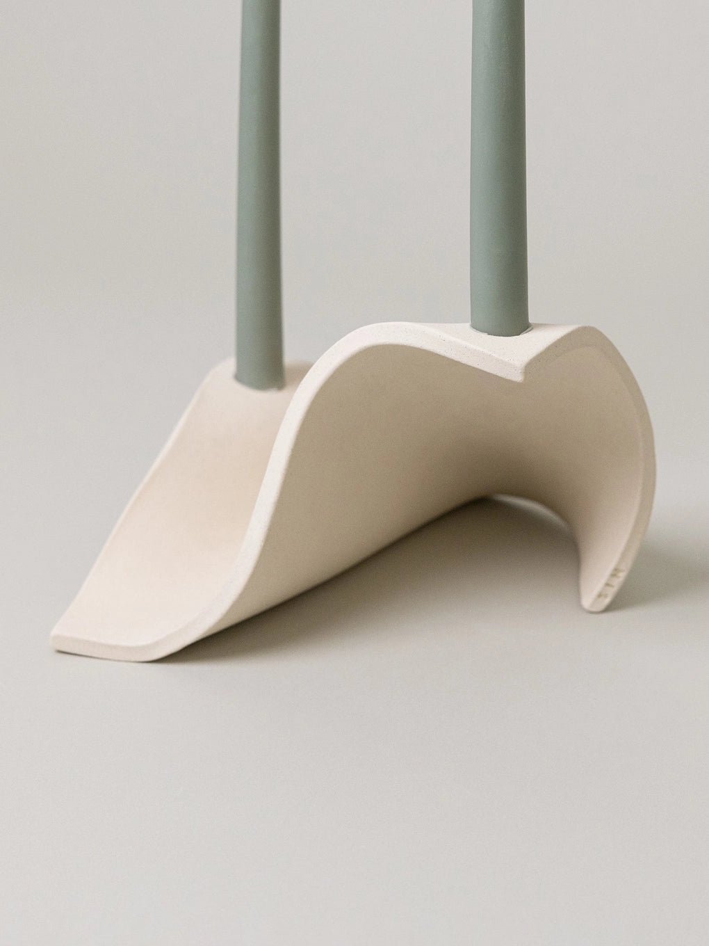 Modern sculptural dual candlestick holder in matte white ceramic with sage green taper candles and organic curved form