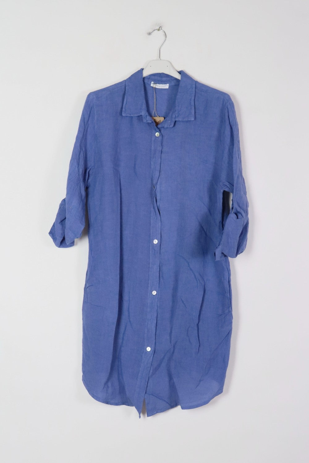 Periwinkle blue linen shirt dress with rolled three-quarter sleeves, white button front closure, and relaxed fit on hanger