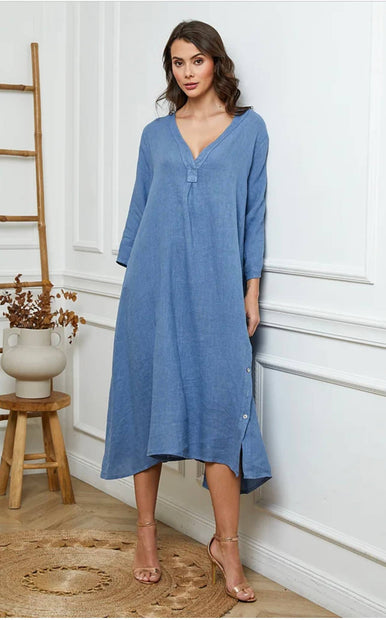 Woman wearing a blue dress standing in a room with white walls and wooden furniture.