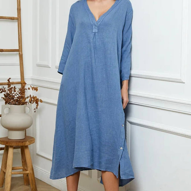 Woman wearing a blue dress standing in a room with white walls and wooden furniture.
