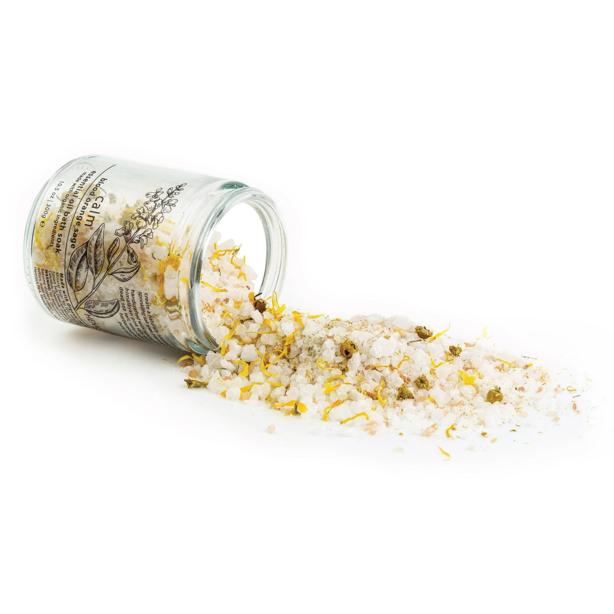 Clear glass jar tipped over spilling botanical bath salts with white crystals, yellow calendula petals, and dried herbs