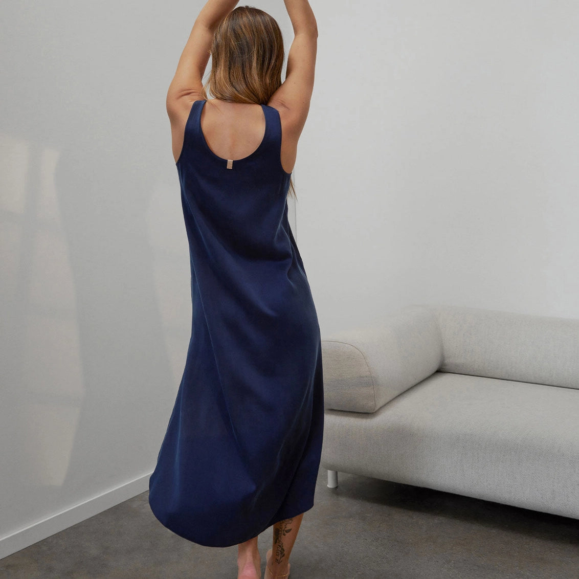 Navy blue sleeveless slip dress with scoop back and gold clasp detail, ankle-length silky drape fabric shown from behind