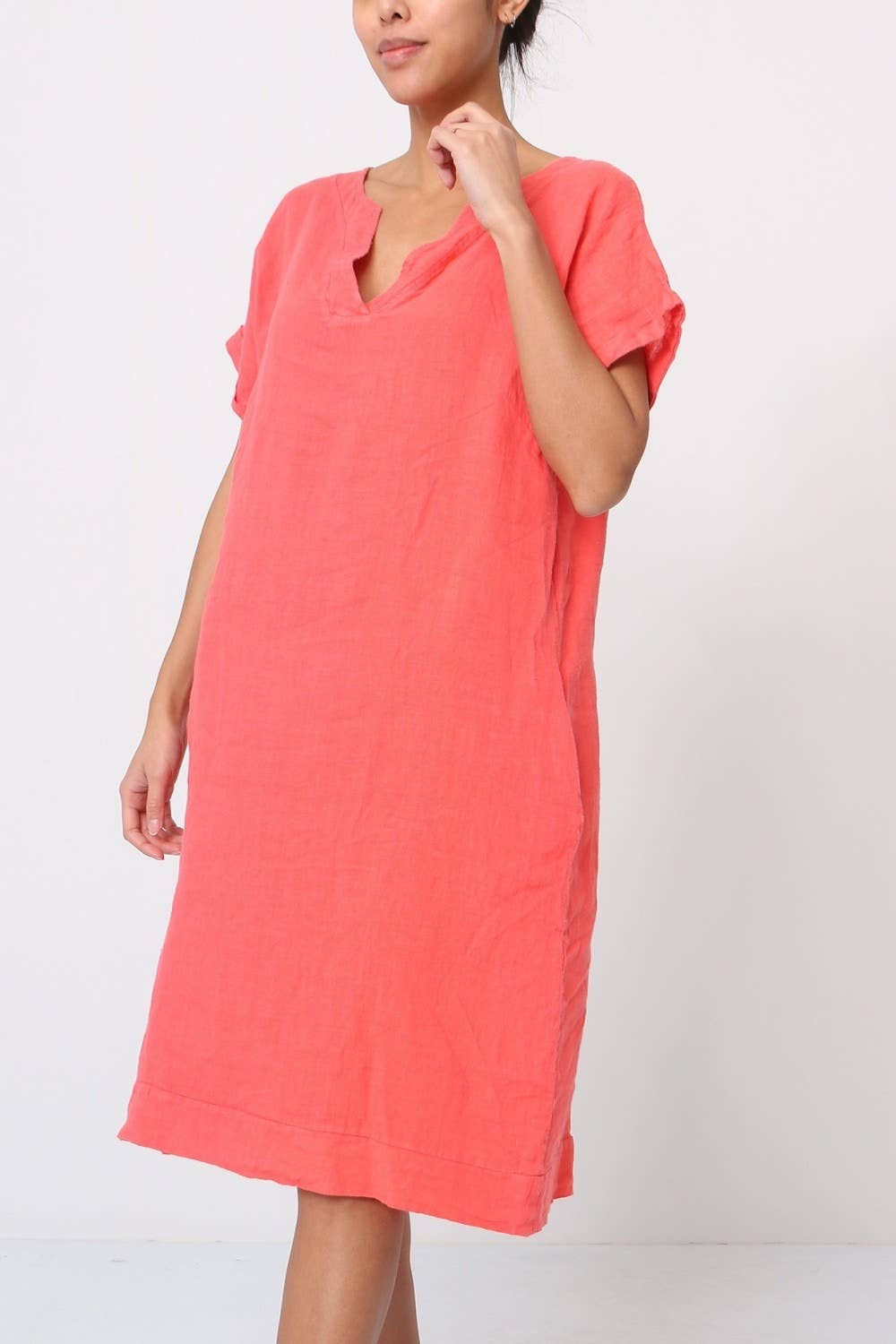 Coral pink linen shift dress with v-neck, cuffed short sleeves, relaxed fit, and knee-length hem on light background