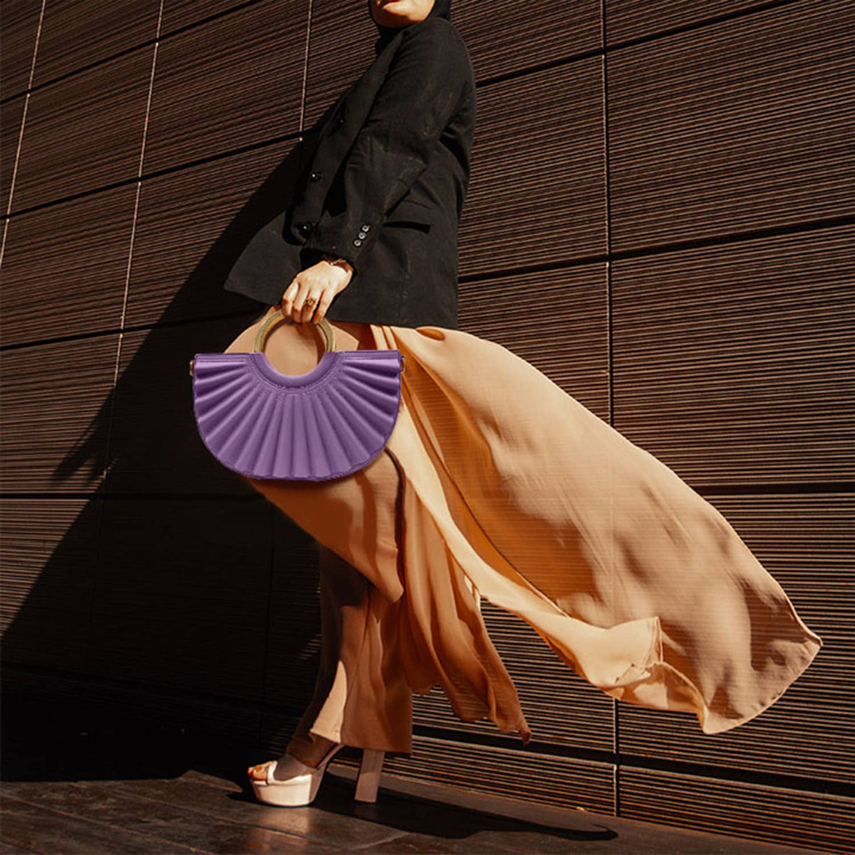Purple pleated half-moon clutch with cutout handle held with flowing golden silk skirt and black blazer ensemble