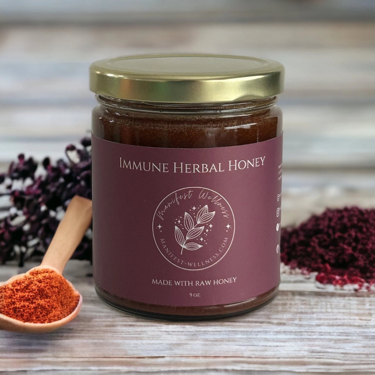 Glass jar of dark brown herbal honey with gold lid and burgundy label, displayed with dried elderberries and spices