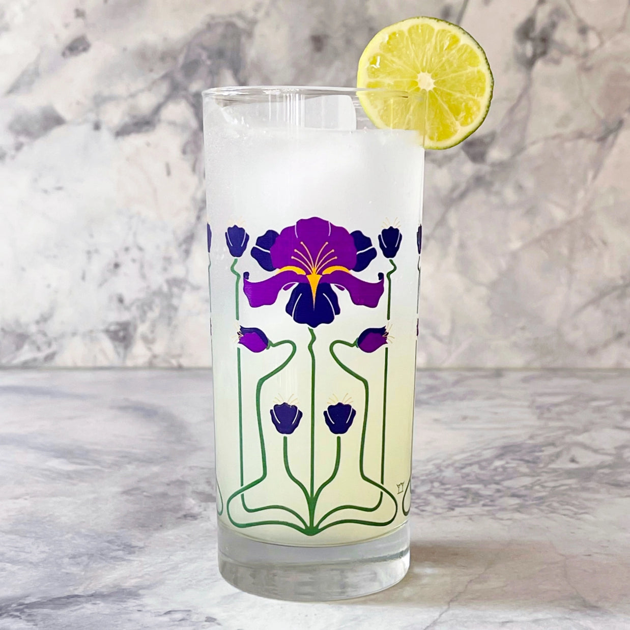 Clear glass tumbler with Art Nouveau purple iris flower design and green stems, filled with lemonade and lime garnish