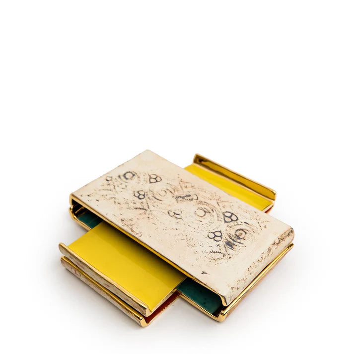 Stack of miniature leather-bound journals with aged cream cover featuring handwritten text, yellow and green page edges visible