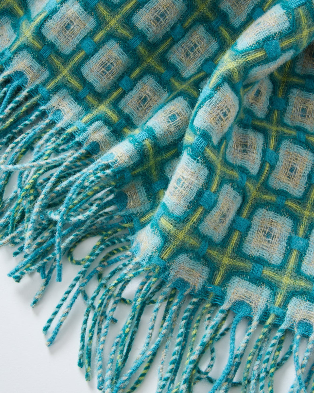 Woven throw blanket with geometric diamond pattern in teal, chartreuse, and cream with twisted fringe trim