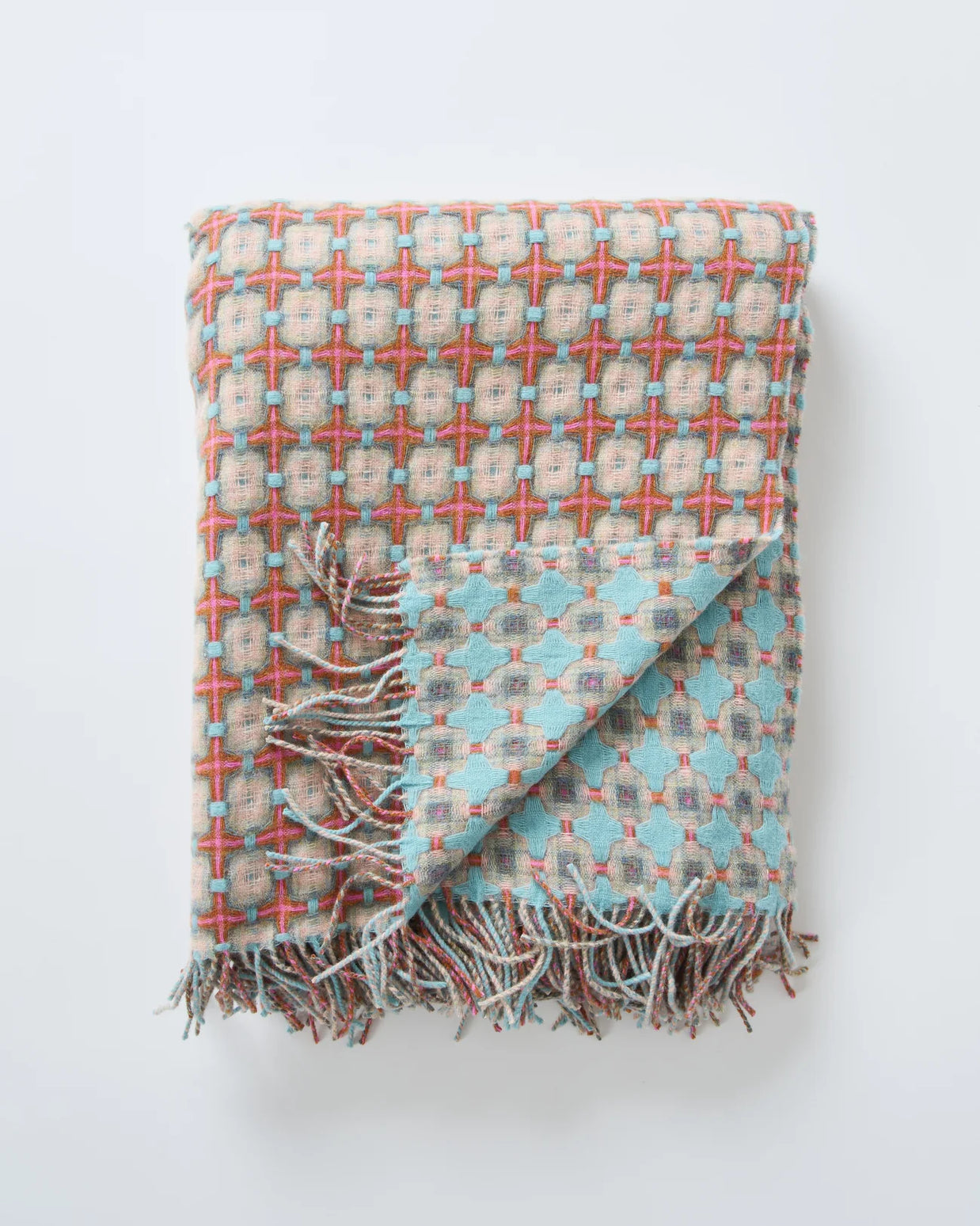 Woven throw blanket with geometric cross pattern in coral, turquoise, and beige with twisted fringe along bottom edge