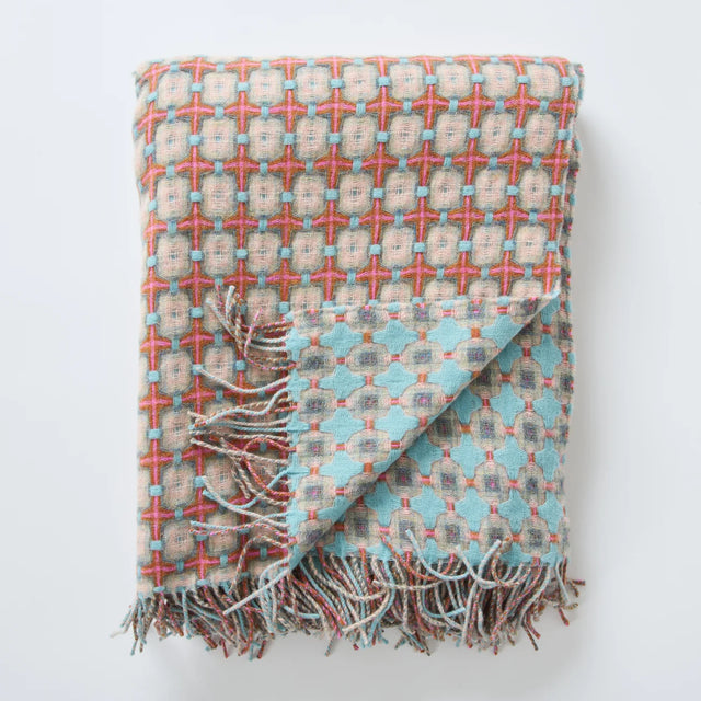 Woven throw blanket with geometric cross pattern in coral, turquoise, and beige with twisted fringe along bottom edge