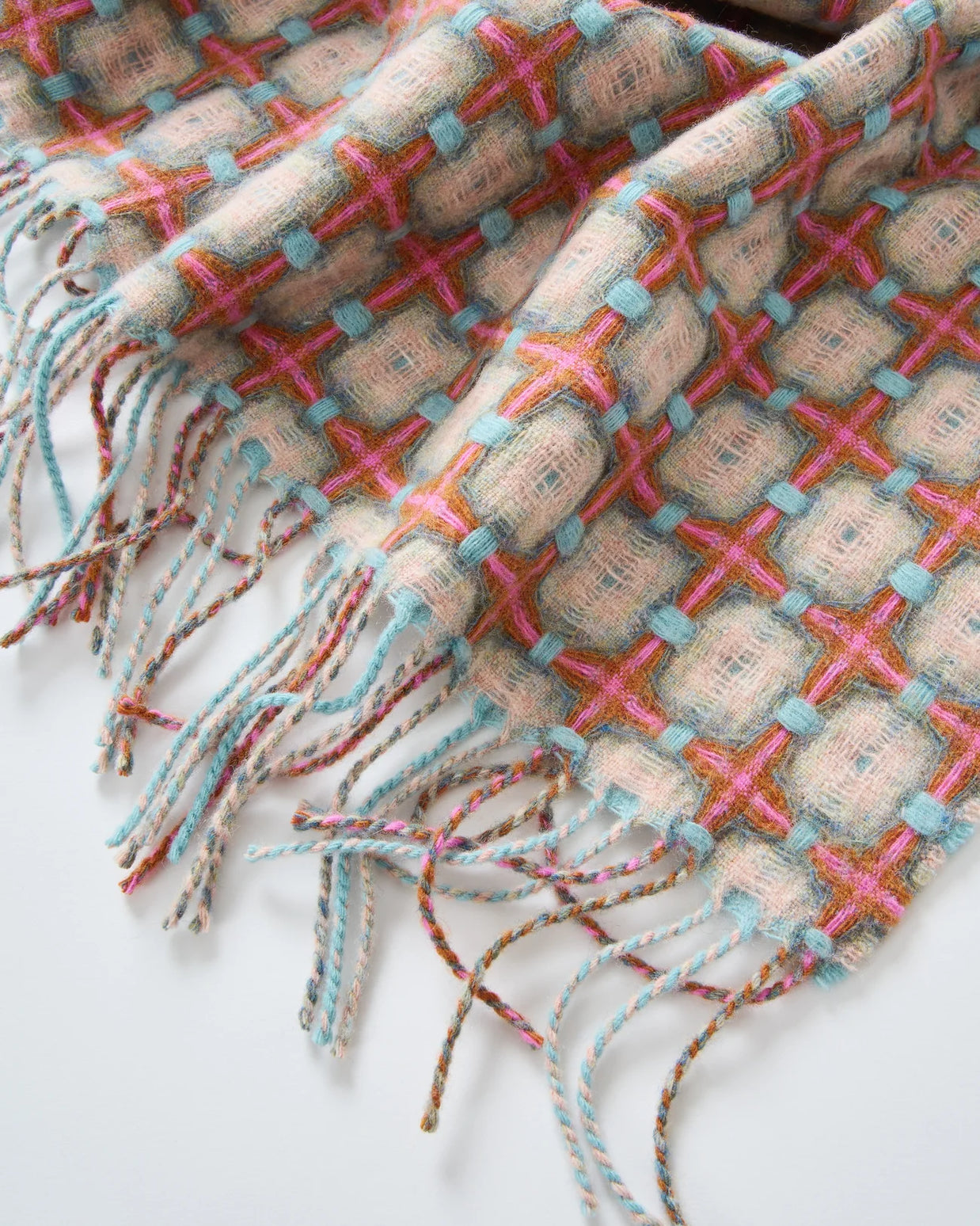 Woven throw blanket in natural beige with colorful cross-stitch pattern in pink, turquoise, and coral with twisted fringe