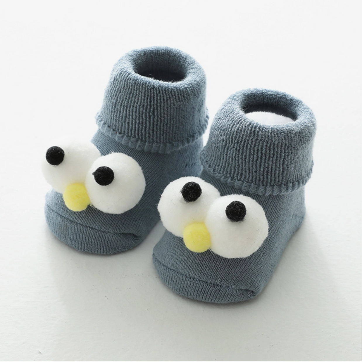 Dusty blue knit baby booties with 3D googly eyes and yellow beak appliqué creating cartoon bird face design