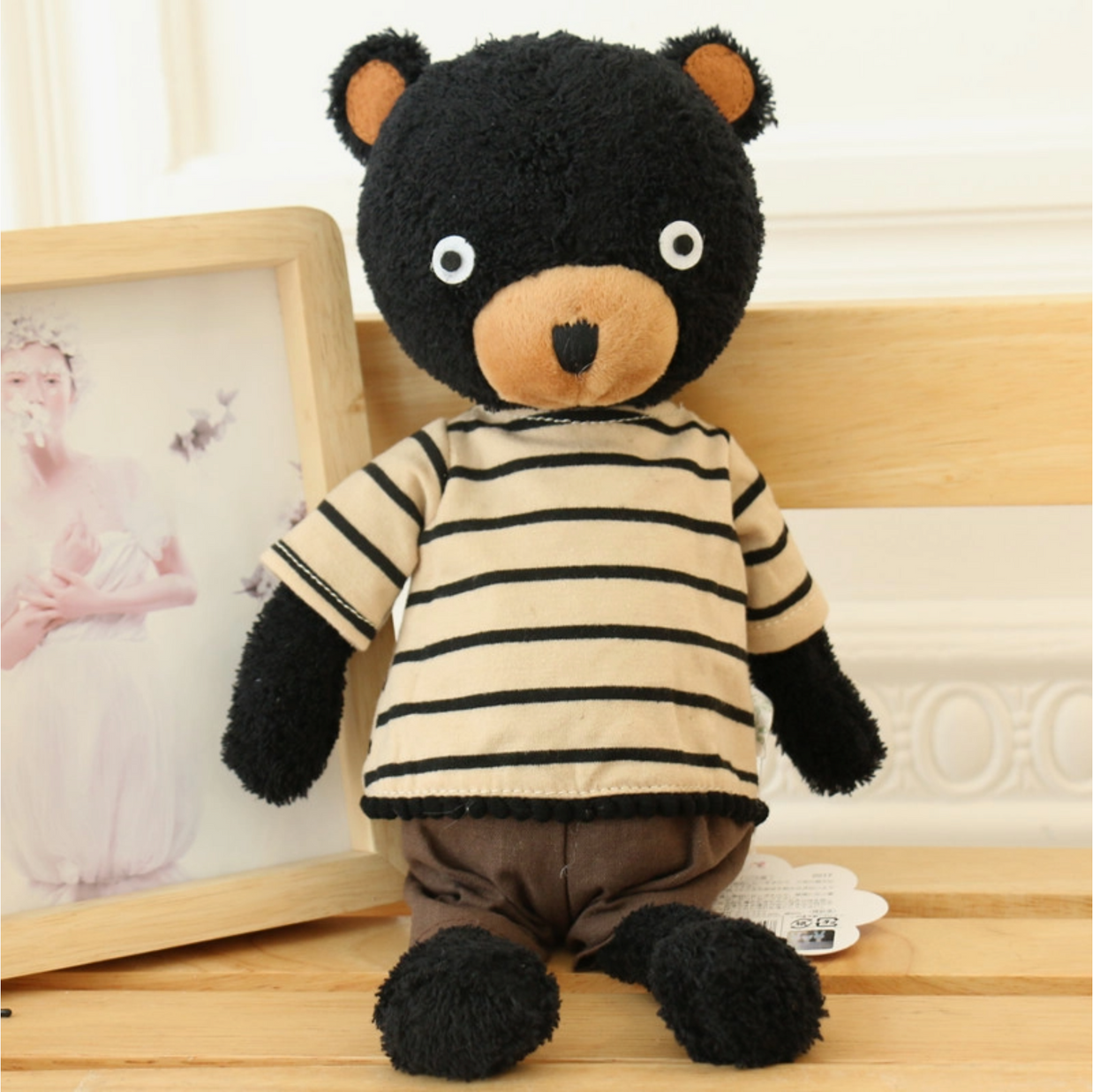 Black plush bear with tan muzzle and inner ears, wearing cream and black striped shirt and brown shorts, sitting upright