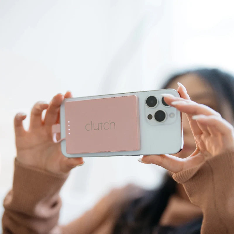 White phone case with dusty rose pink wallet attachment labeled clutch, held by person taking photo in beige sweater