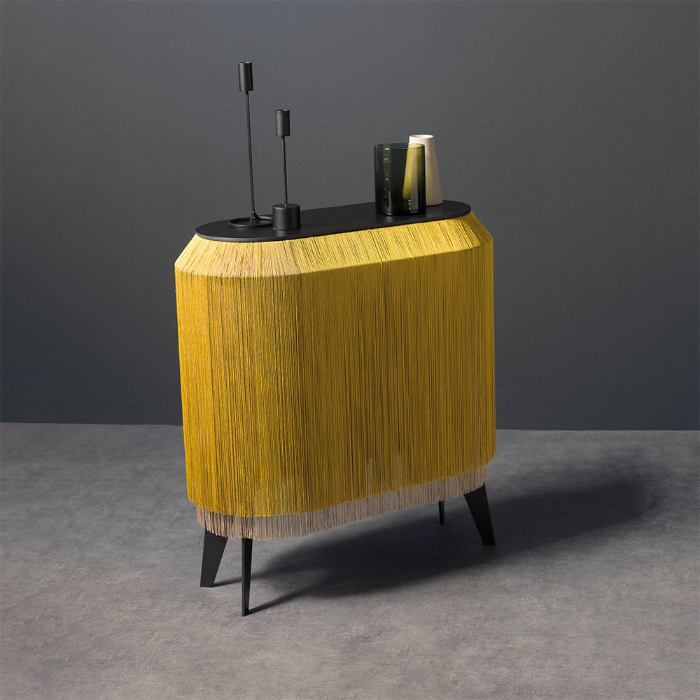 Modern oval bedside table with black top, golden yellow fringe trim, and angled black legs, styled with candlesticks and books